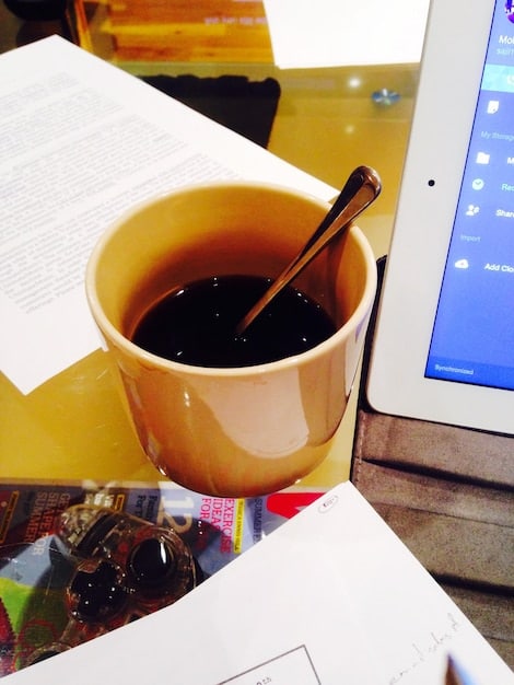 A close-up of a tax form being filled out with a pen. A calculator and a cup of coffee are also visible, suggesting the task of financial planning.